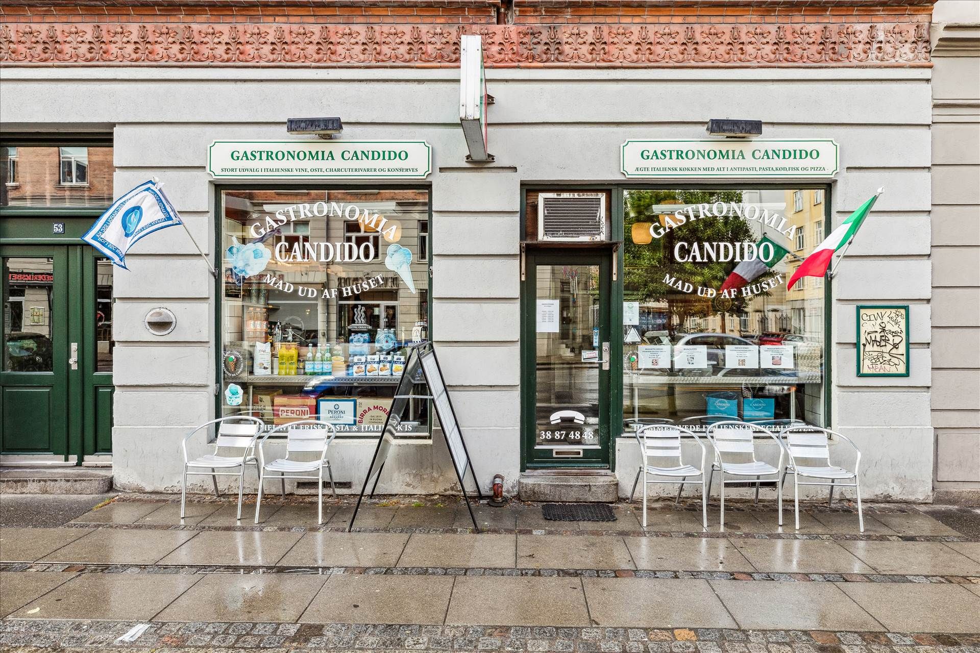 En italiensk delikatesseforretning med navnet Gastronomia Candido og stolpe med flag og skriftstykker foran