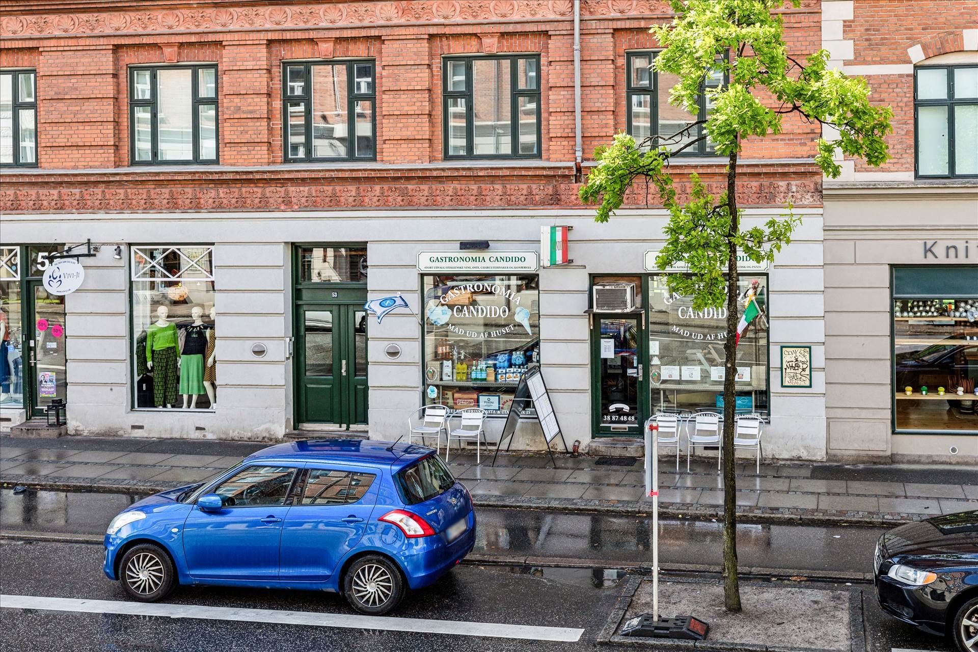 En blå Suzuki Swift parkeret foran en bygning med røde mursten og vinduer, hvor det er skiltet Gastronomia Candido