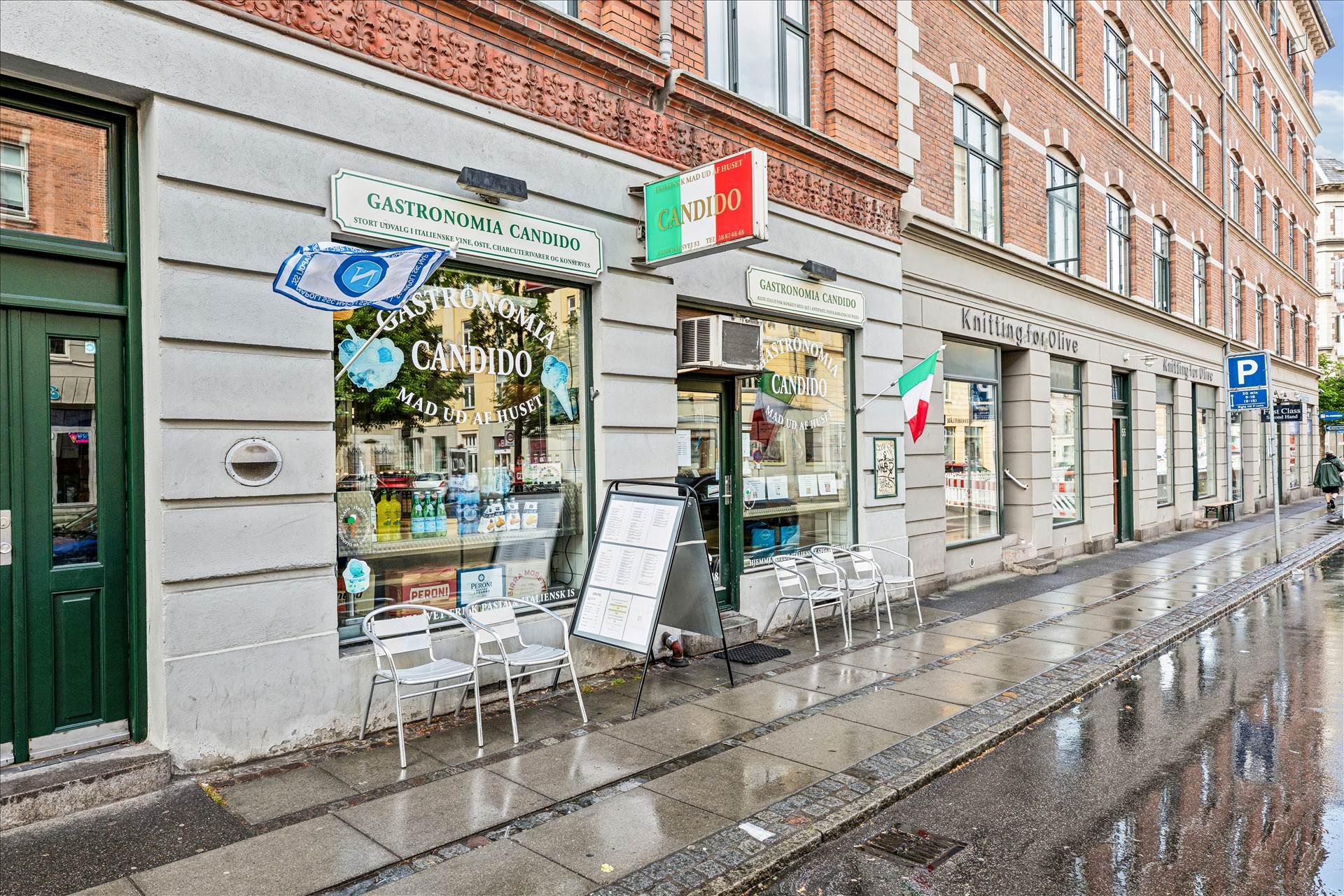 Regnvand på en gågade foran en italiensk restaurant med grønne døre og en række møbler