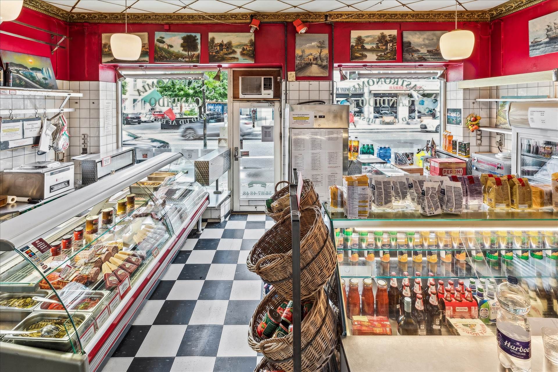 Køkkenudstyr og salgsreoler med varer, øl og flasker i en italiensk delikatesseforretning med røde vægge og tæppegulv
