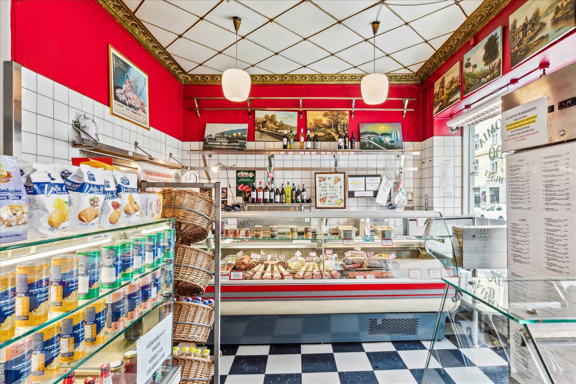 Indvendigt i en delikatesseforretning med røde og hvide vægge, krydrede produkter, kød og pølser i udskærmning og flere