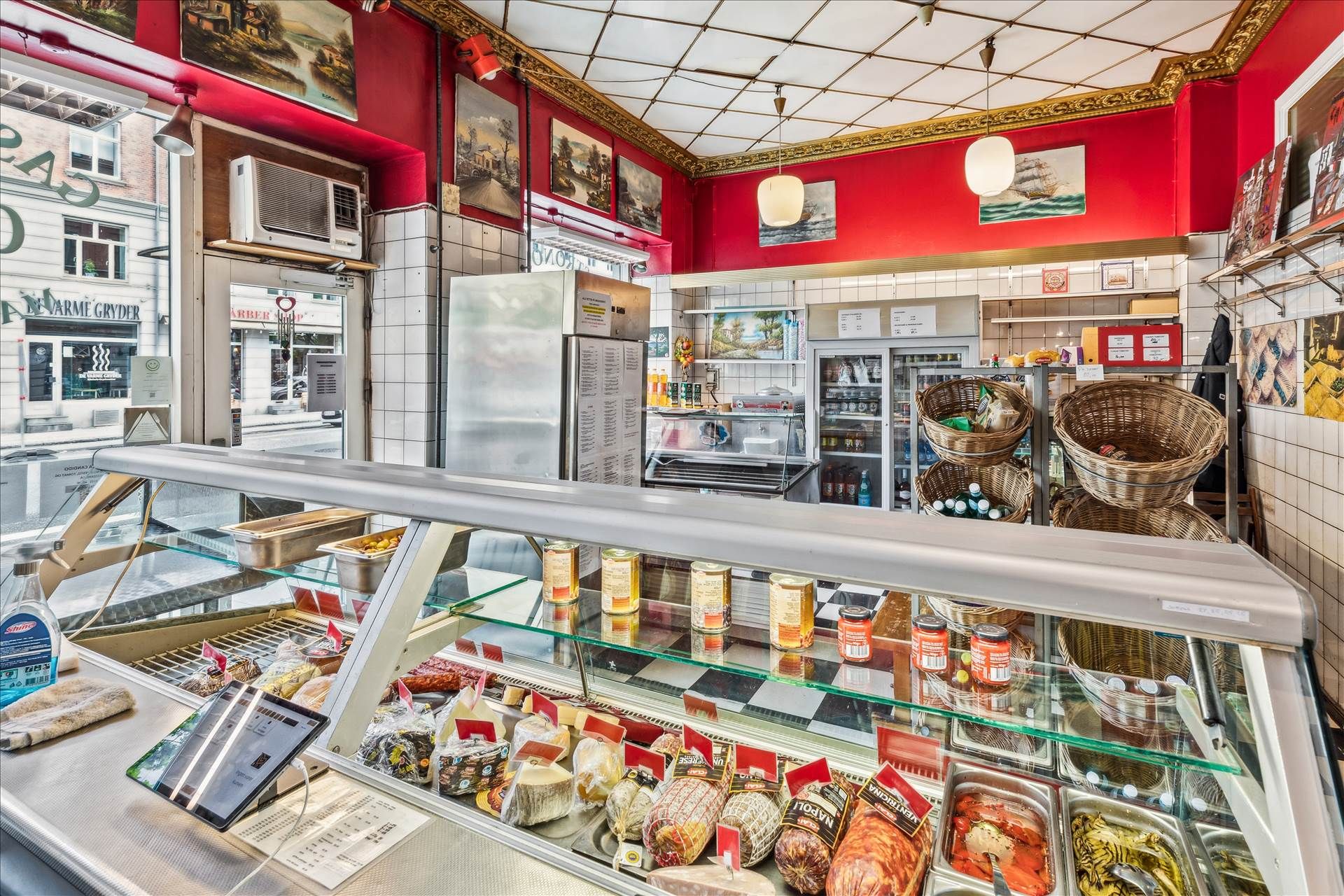 En italiensk delikatesseforretning med mange forskelige varer som kød og ost i udstillingsskuffer og flere kurve med