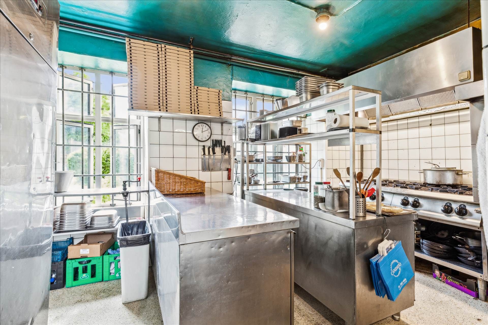 En ren og funktionel køkkenindretning med store ståloverflader, stålreoler, spisestuebord, apparater og udstyr samt en stor