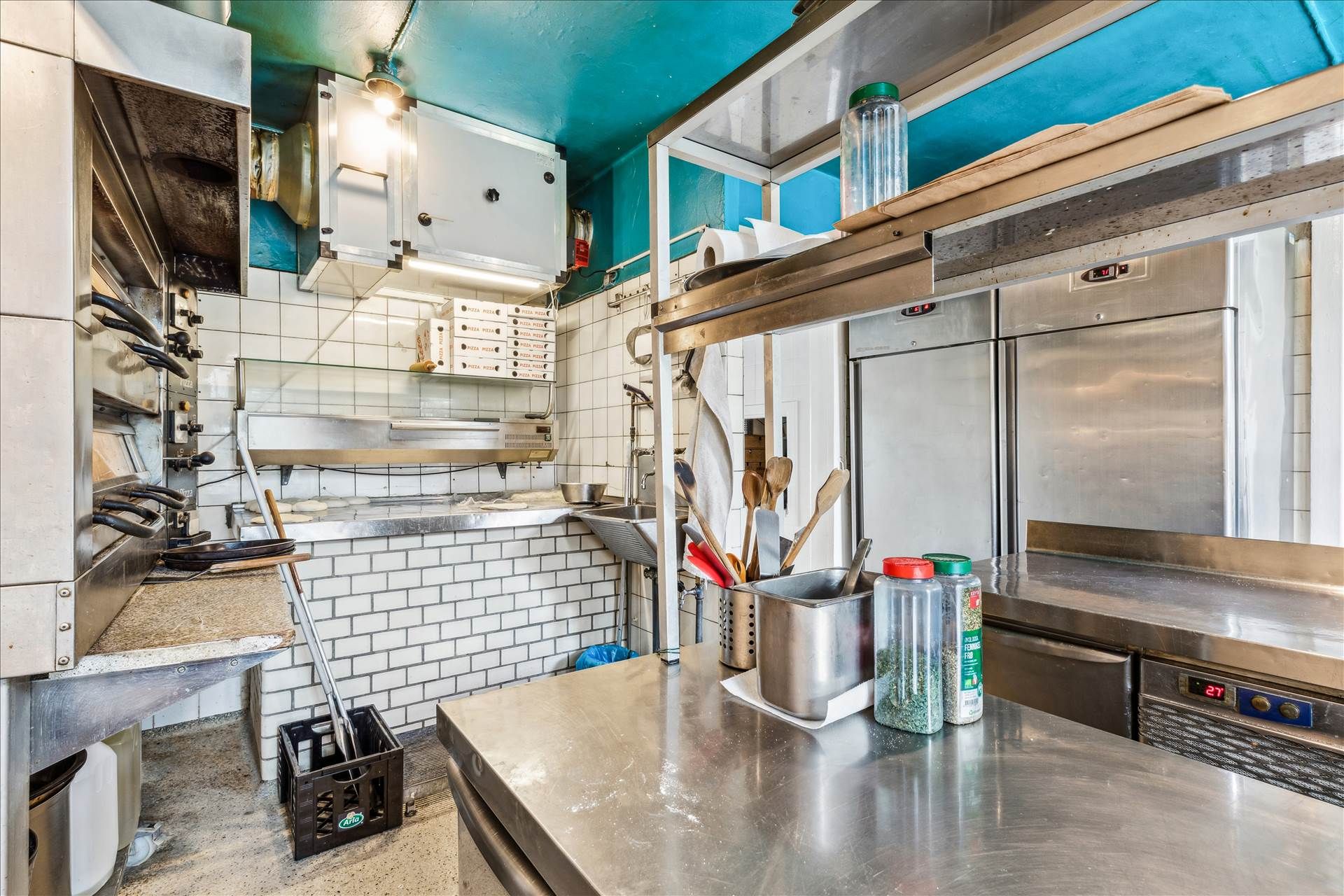 Køkken med renser, køleskabe, rustfri stålbord, krydderiglas, og brændende lampe over loftet i en delikatesseforretning