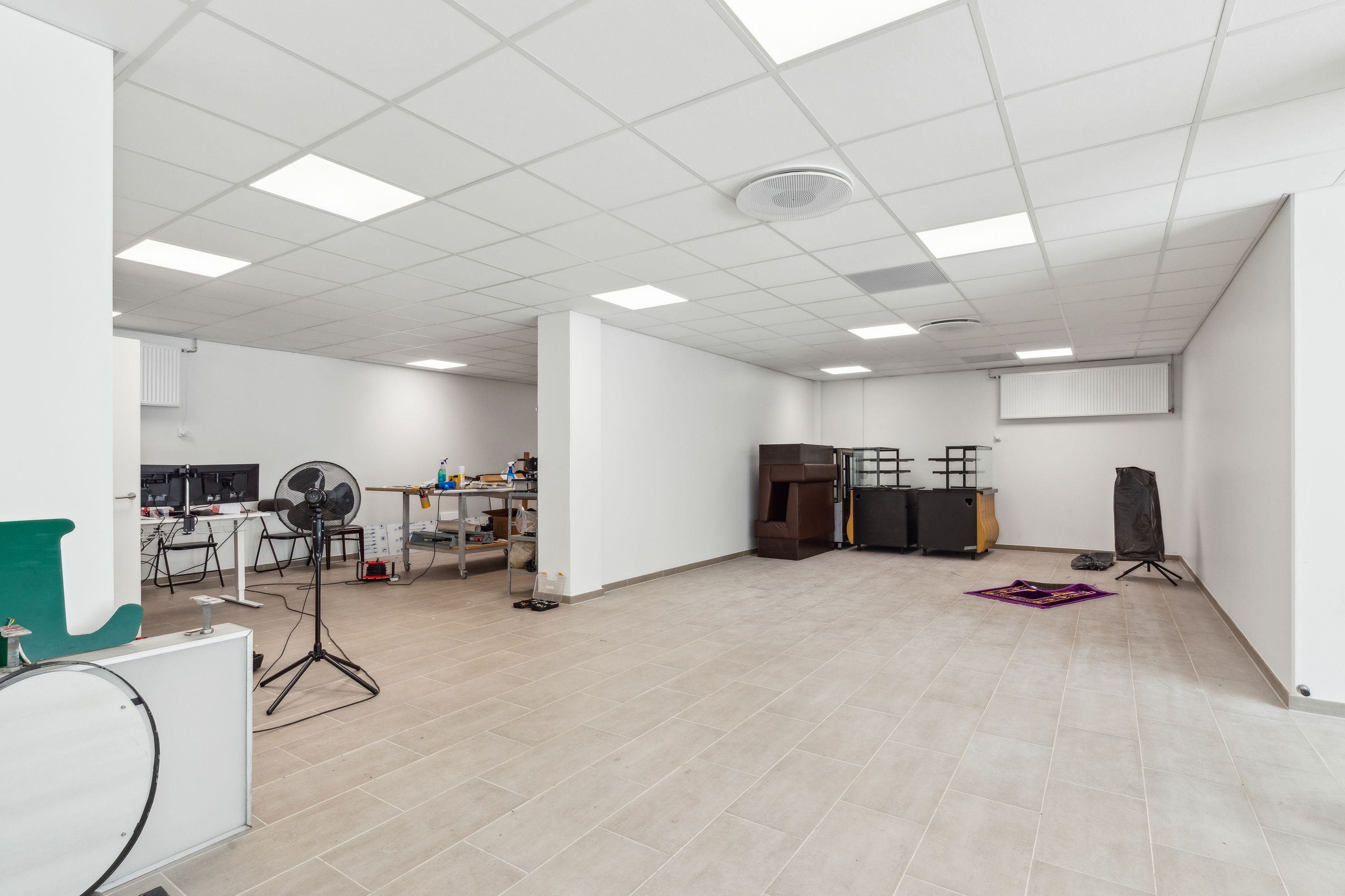 En tom stue med lysegult gulv og hvide vægge. Værelset er delt af en høj væg og indeholder diverse udstyret, herunder en