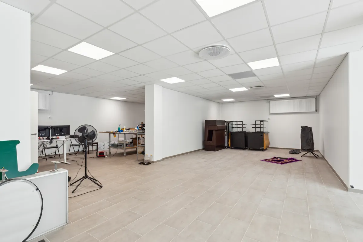 En tom stue med lysegult gulv og hvide vægge. Værelset er delt af en høj væg og indeholder diverse udstyret, herunder en