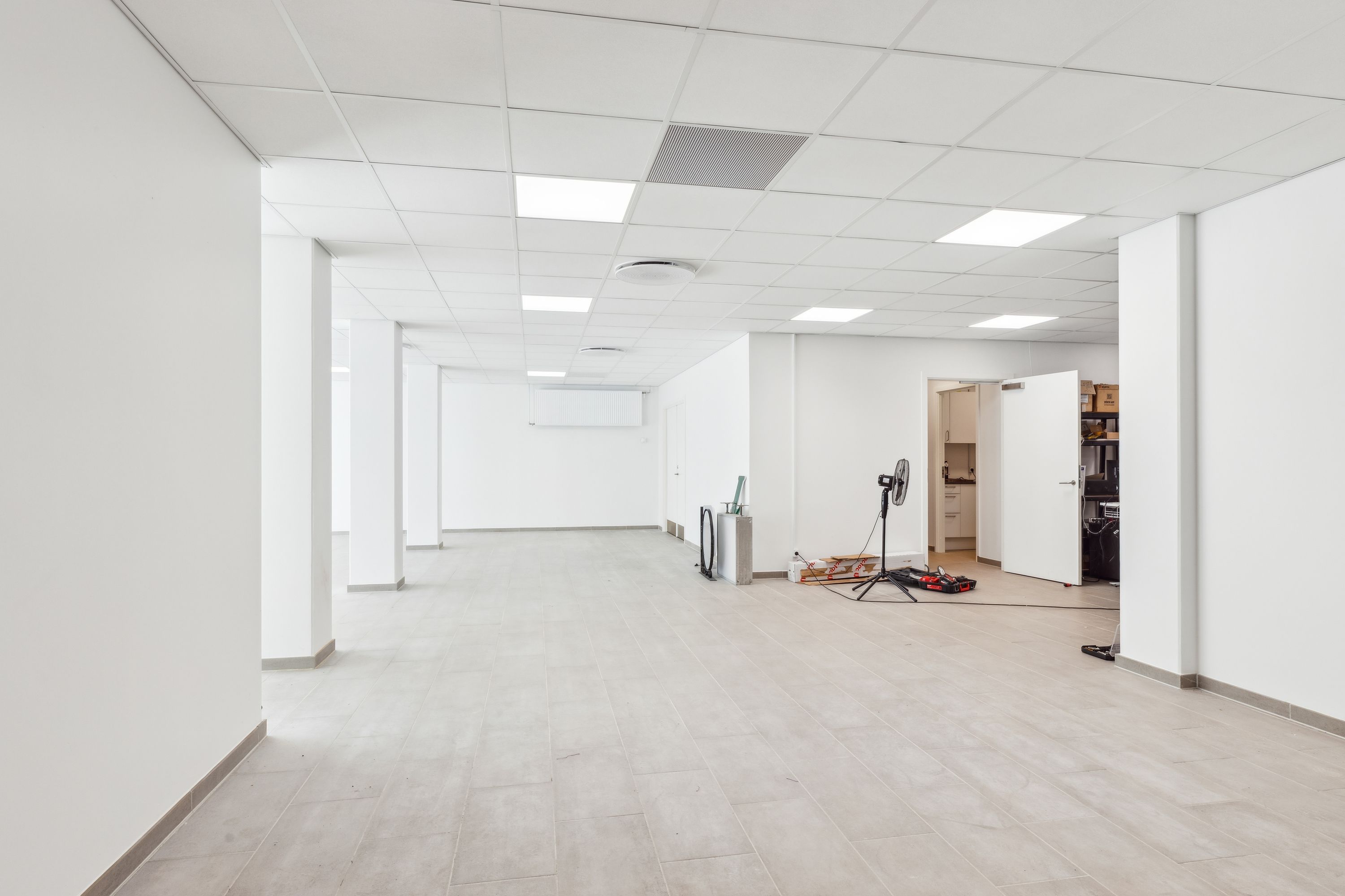 Et tomt kontor med hvide vægge, loft og gulv, samt flere hvide søjler og en åben dør