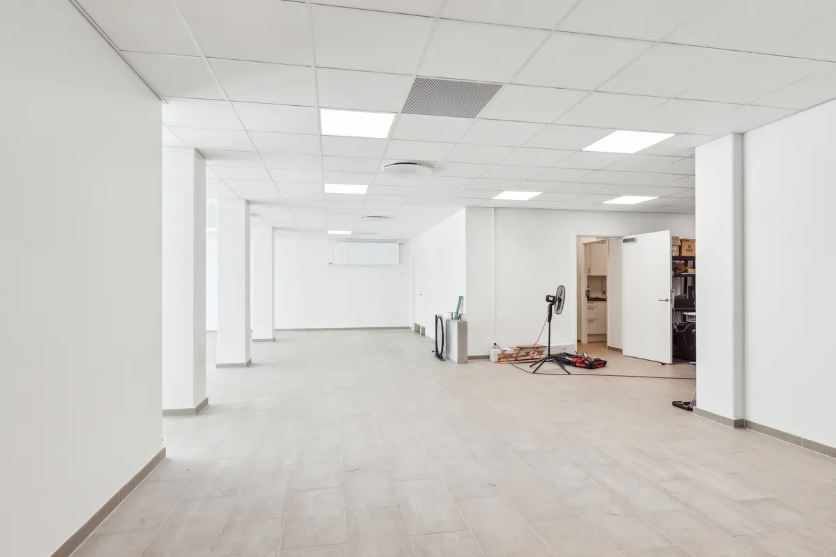 Et tomt kontor med hvide vægge, loft og gulv, samt flere hvide søjler og en åben dør