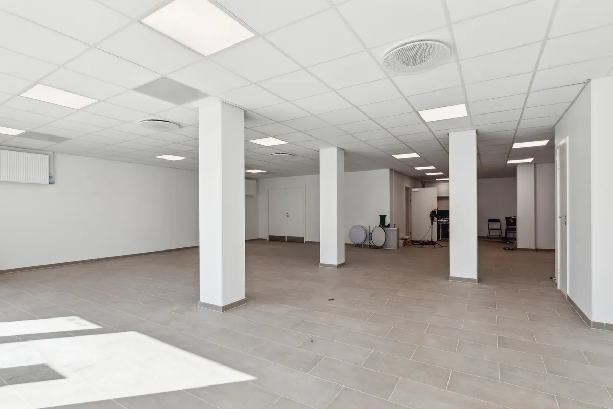 En stor, lys, tom stue med hvidt loft, hvide vægge og gulv med lysegrå fliser. I hjørnet er der en garderobe og en åben dør.