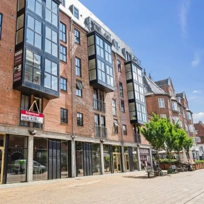 Bryggergården er en ny lejemål i Odense City. Bygningen med store glasruder er nyrenoveret. På gaden er der bænke og træer.