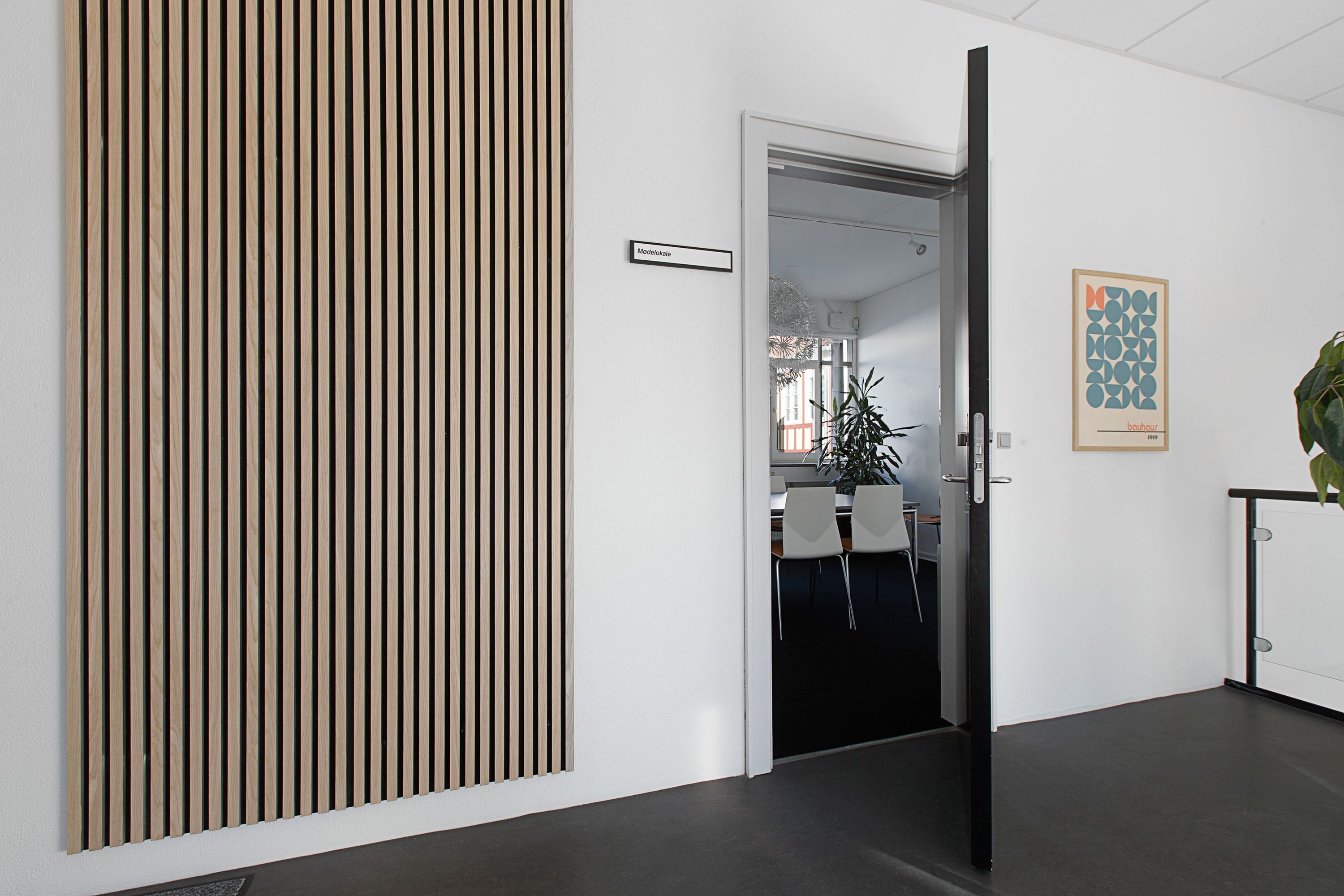 Kontor med åben dør og teksthængslet, lysegul væg, stribet vægpanel, stol, plante, maleri og gulvbelægning