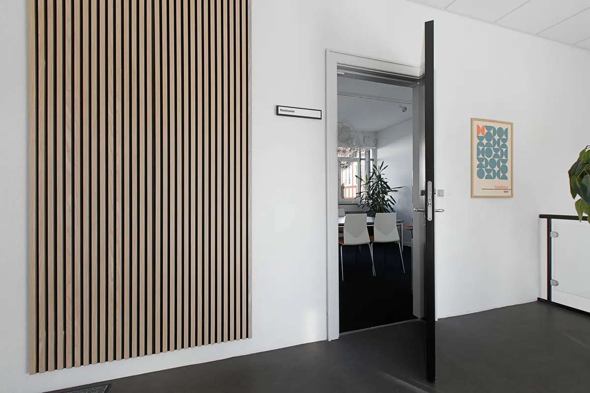 Kontor med åben dør og teksthængslet, lysegul væg, stribet vægpanel, stol, plante, maleri og gulvbelægning