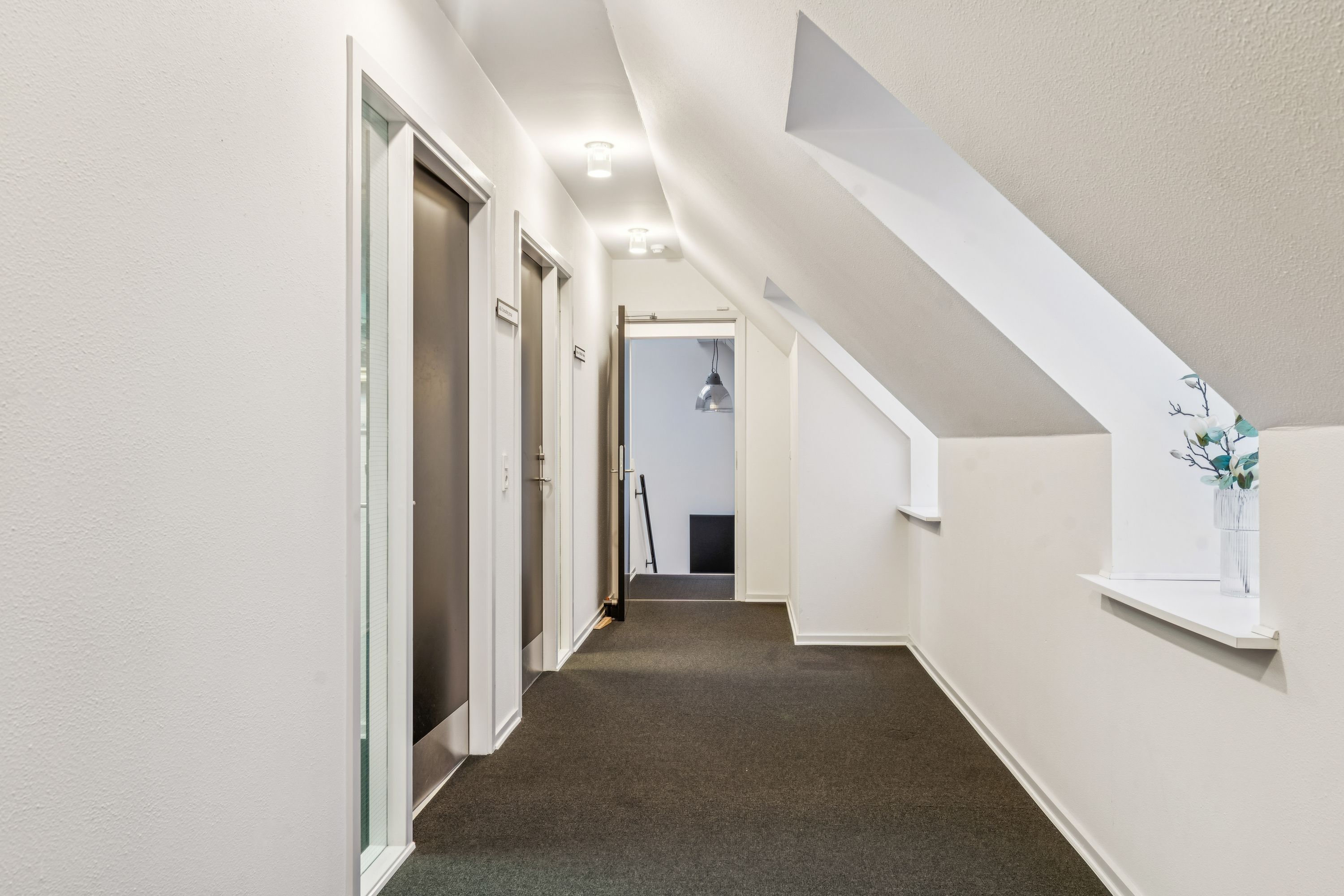 En lang, mørk korridor med hvide vægge og lofter og en høj gulvbelægning med slanke hvide vinduesruder