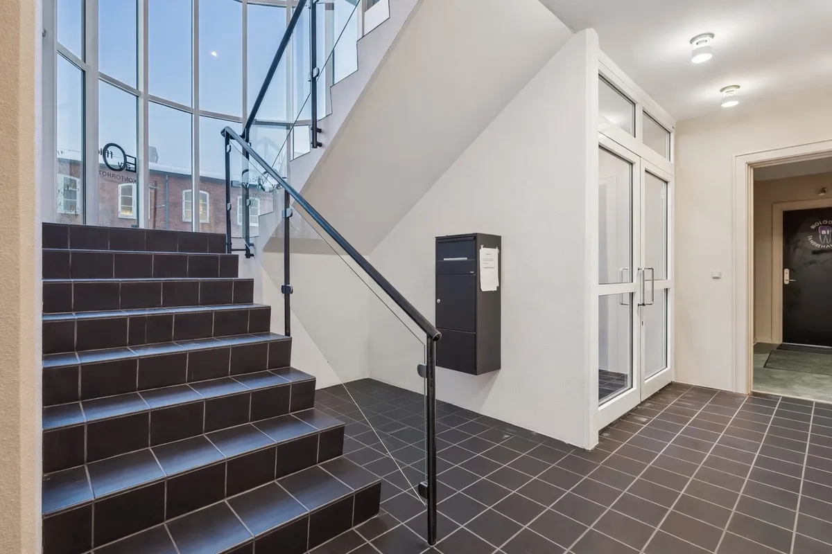 Støbejernsgesims og moderne trappe med sort bestrukne trin og skravede håndtag samt to kabiner placeret på væggen