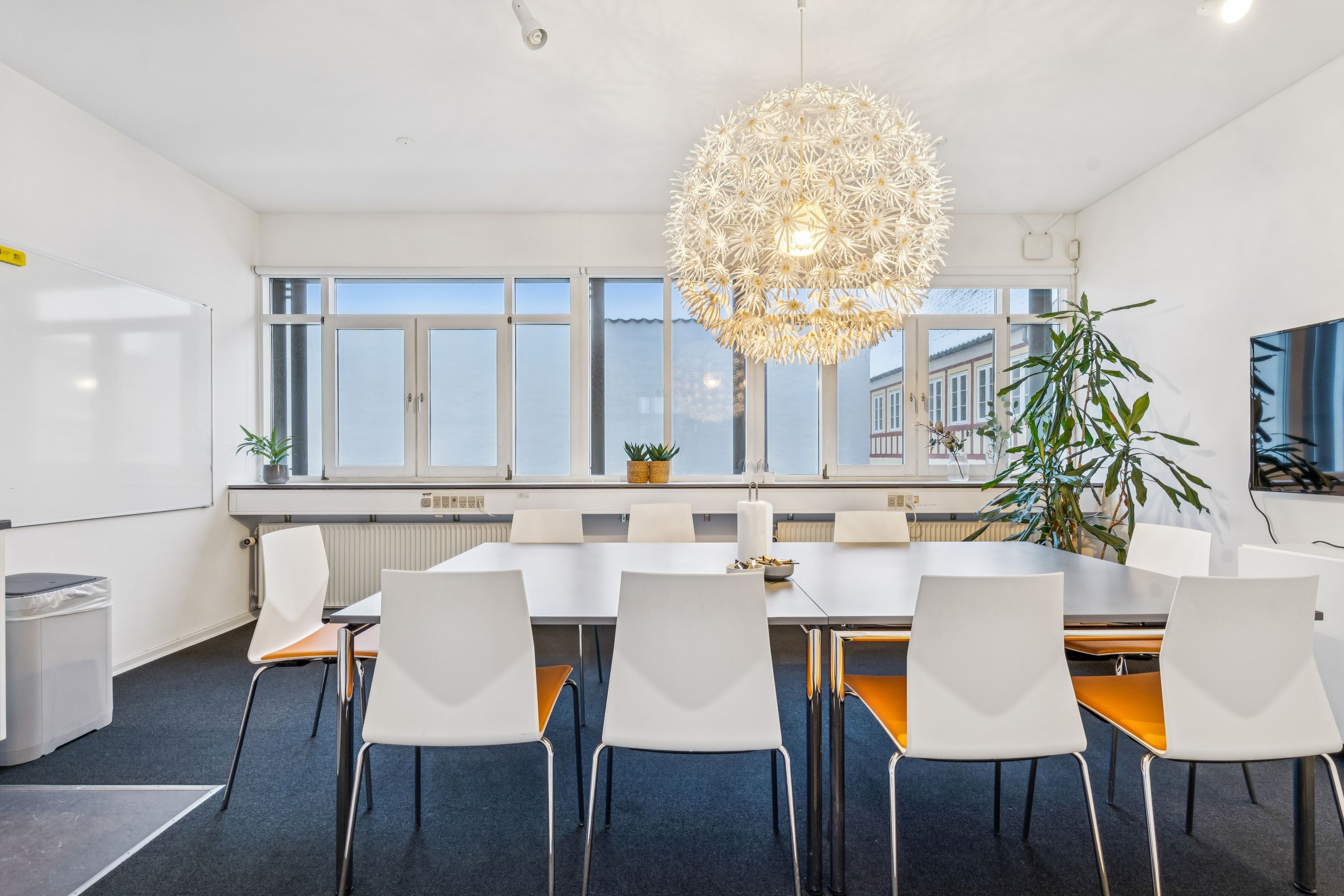 Kontorrum med stort møbelbord, lysegul blomsterlampe og lysegule stole samt plante og tv på væggen