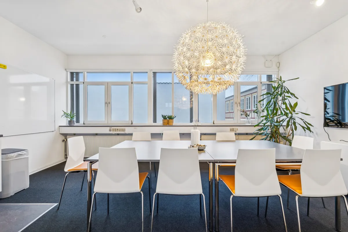 Kontorrum med stort møbelbord, lysegul blomsterlampe og lysegule stole samt plante og tv på væggen