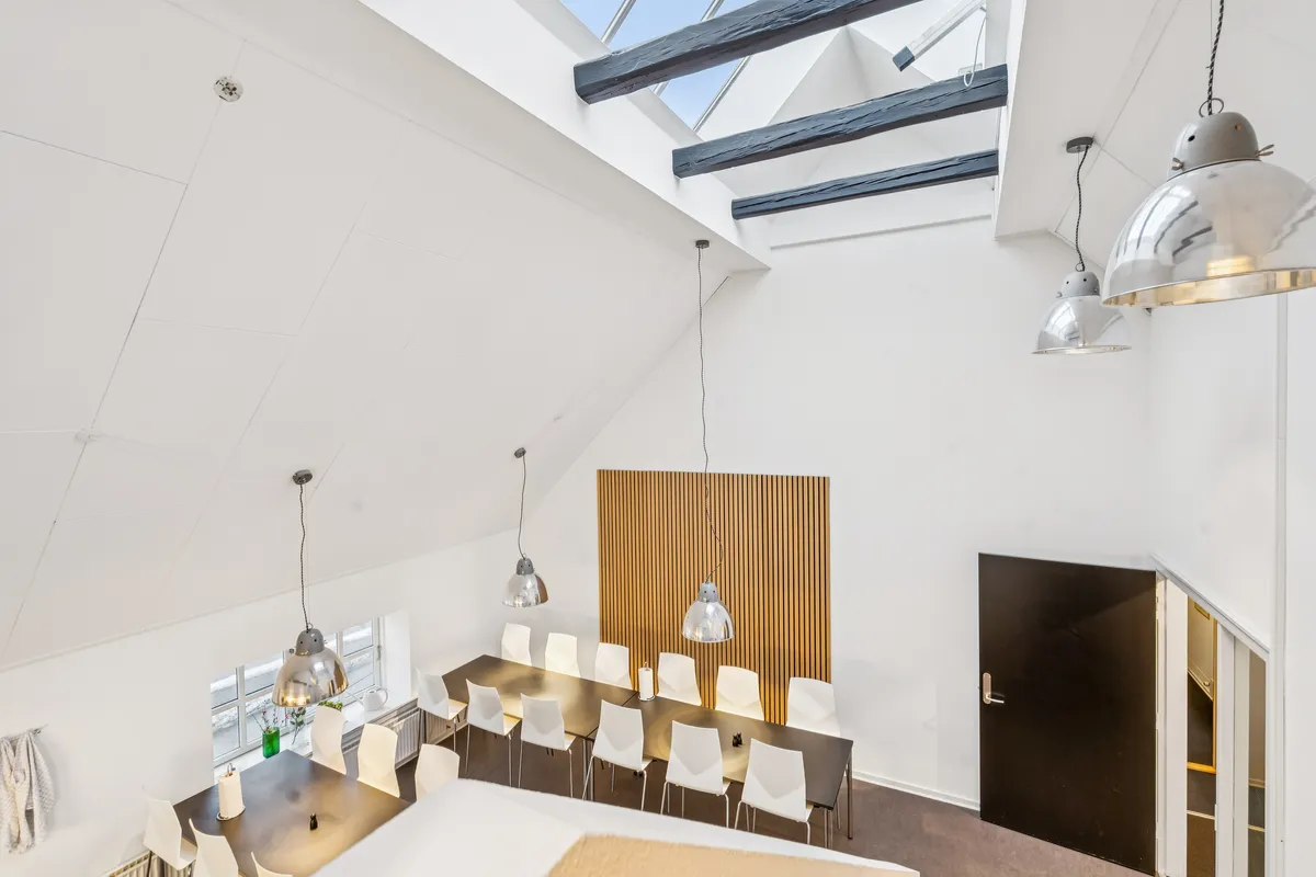 Kontorfællesskab med mødelokaler og bord med stole i loftet og moderne interiør med lyse loftsvinduer og store lysekroner