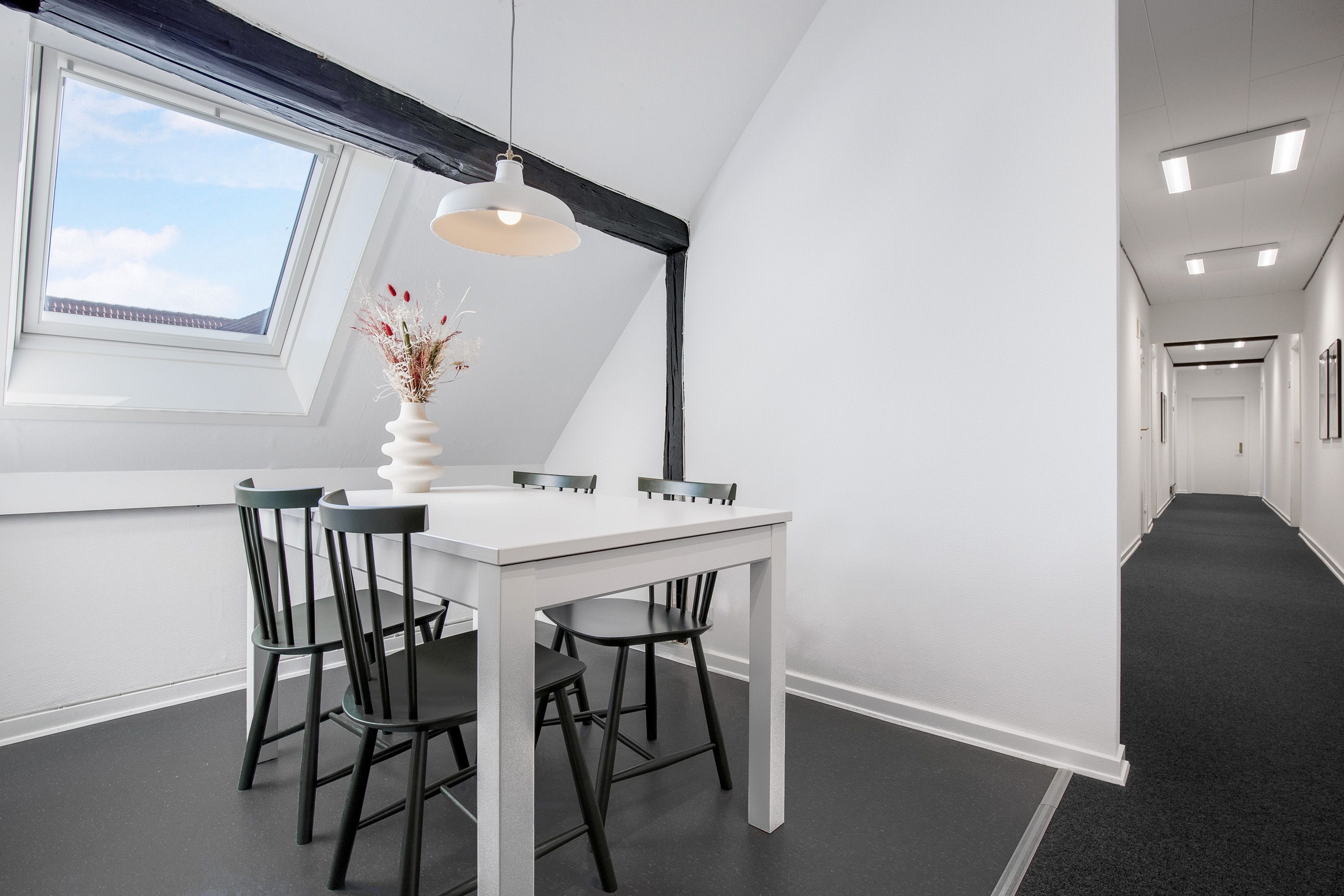 Lej et kontorlokale med lyse hvide vægge, mørke gulve og en stor hvid bord med lyserøde blomster i en vase.