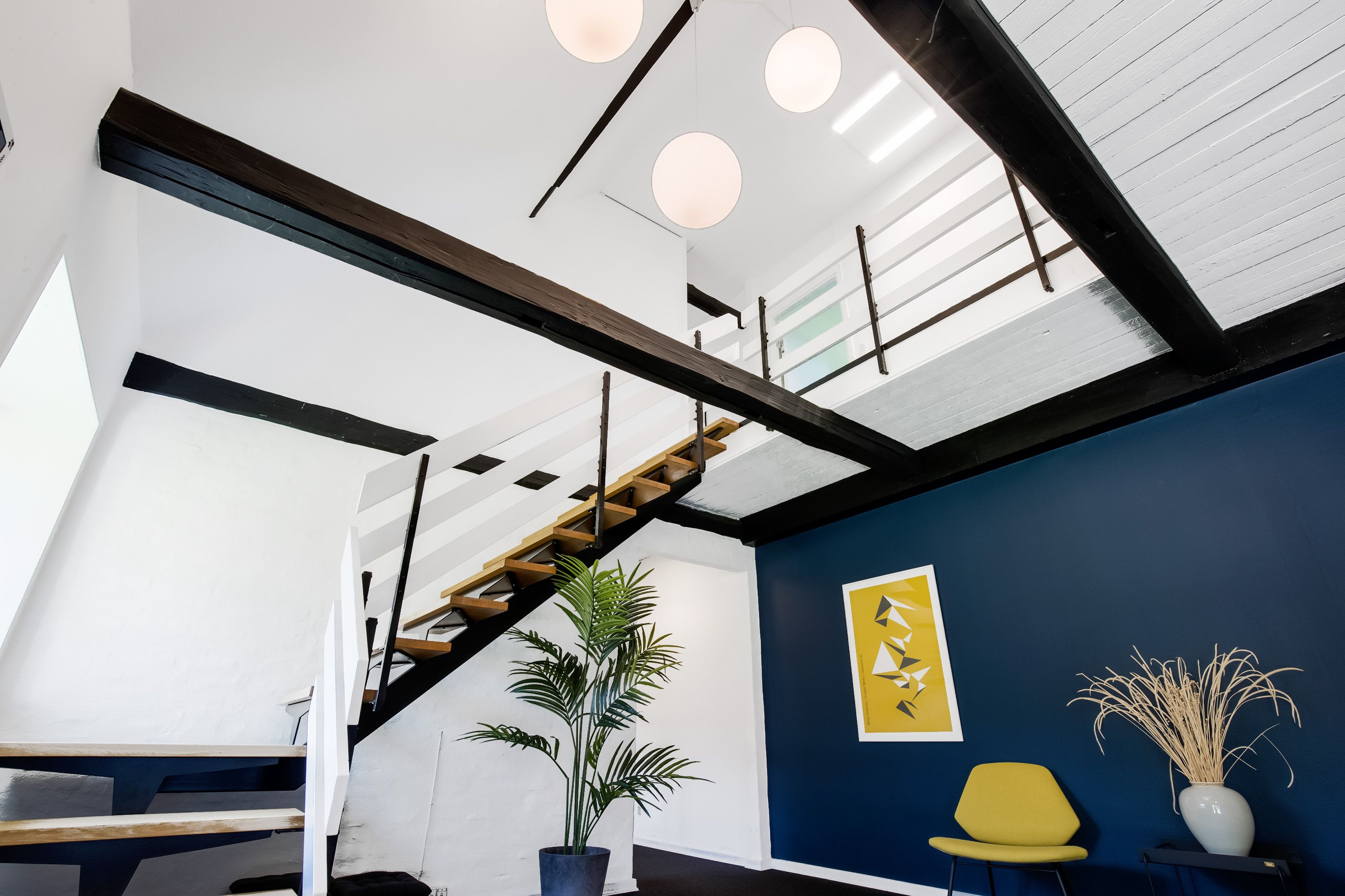 Kontorlokale med loftsvinduer og lysekroner, hvor en sofa og plante står ved den blå væg med et billede