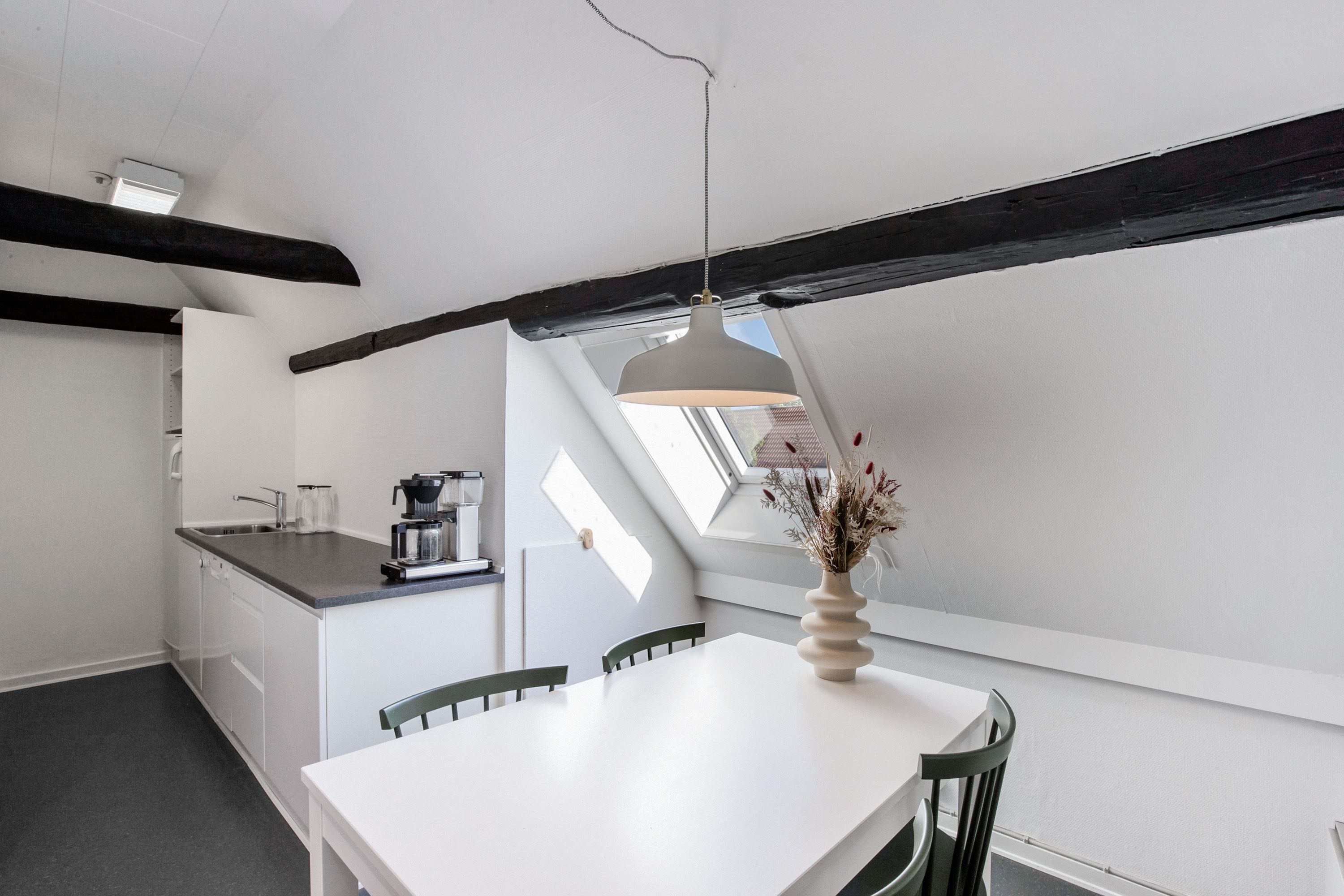 En lille køkken og spiseområde med en hvid bord og stolen og et hængende lampe over bordet og et vindue med udsigt til en