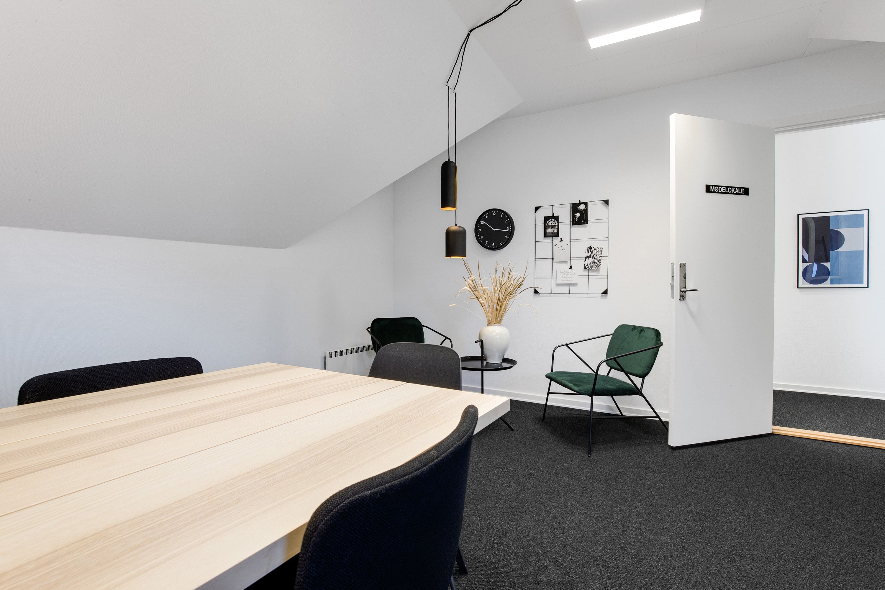 Kontorlokaler med moderne møbler og højloftet. Der er en lang bord og fire stole samt en dør og et billede på væggen