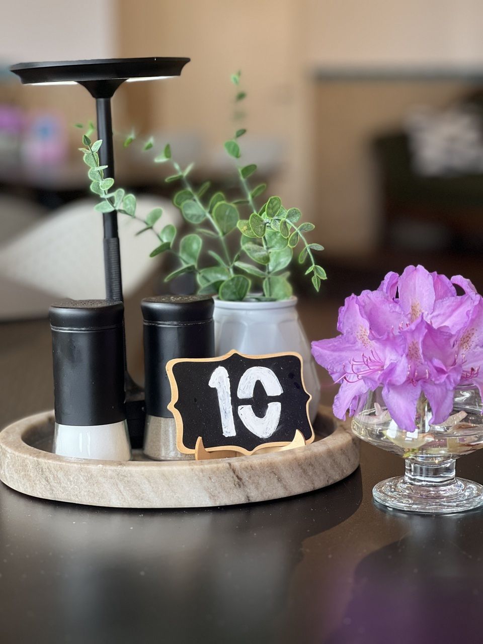 Bord med nummer 1C, to sort-hvide salt- og peberflasker, en grøn plante i hvid vase og en vase med lilla blomster på