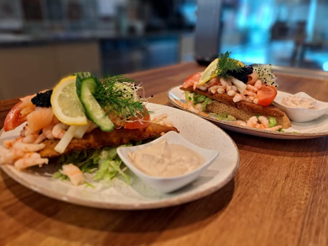 To lyserøde tallerkener med marinereret røget laks og røget fisk placeret på en brun bordplade med krydderurter og salat