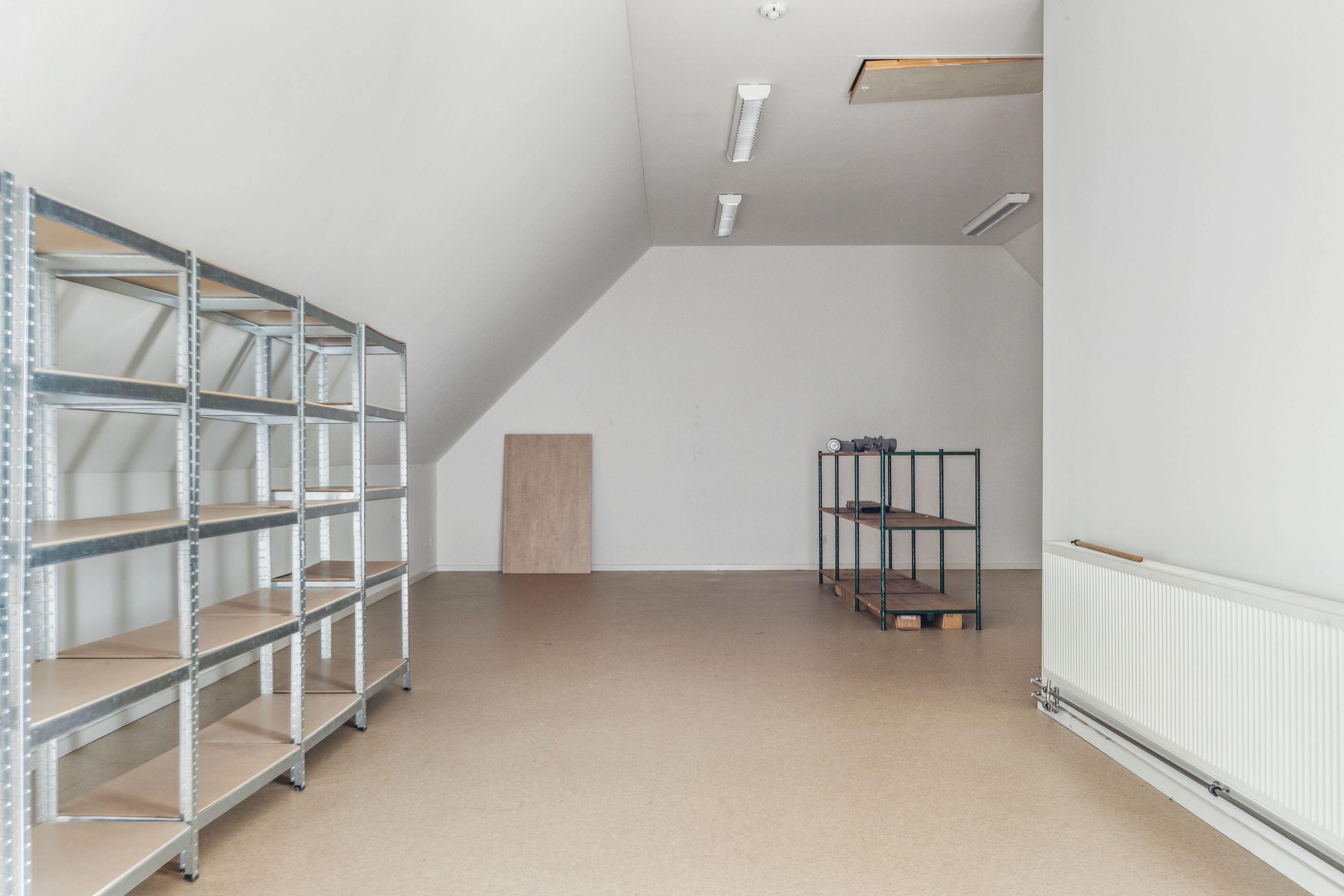 Værelse med to hylder, højloft, lyspærer, et stykke træ og et hvidt varmeapparat i højre side af rummet