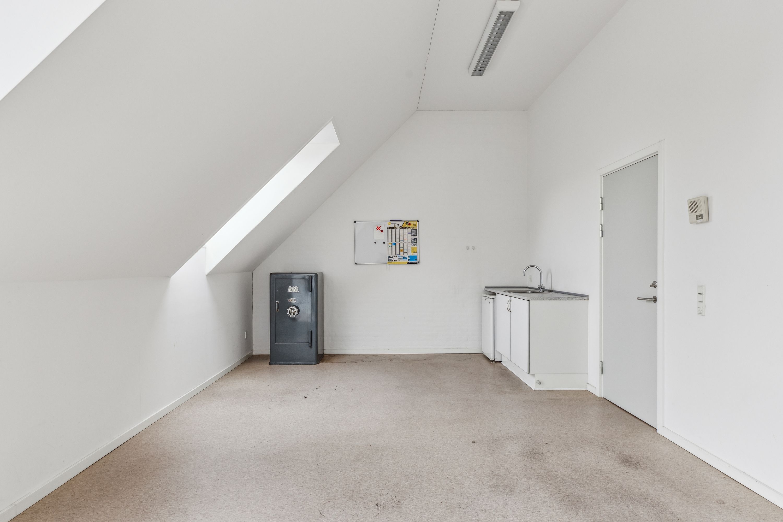Et tomt kontorlokale med en hvid væg og loft samt en lille hjørnekøkken med hvidt køkkenskab og håndvask samt et gulvtæppe