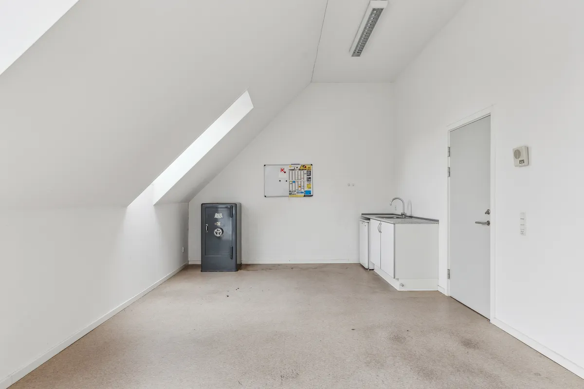 Et tomt kontorlokale med en hvid væg og loft samt en lille hjørnekøkken med hvidt køkkenskab og håndvask samt et gulvtæppe
