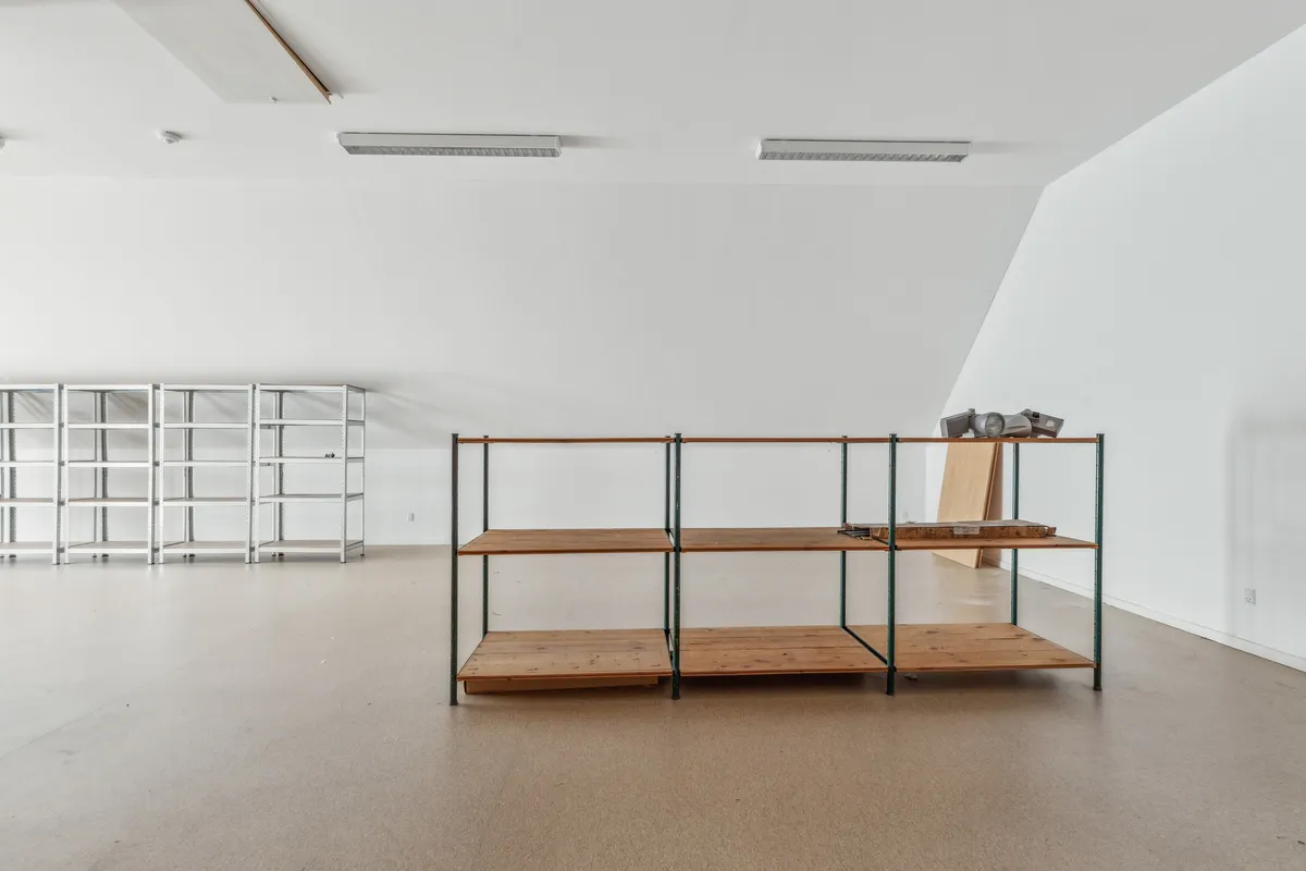 En stor rummelig lagerhal med hvide vægge, to store metalliske hylder og en tredelt træhylde med træplanker