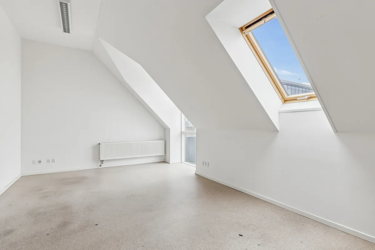 Et hus med en hvid væg og loft og en åben loftsvindu med udsigt til et blåt himmel. Værelset er tomt og har en hvid radiator