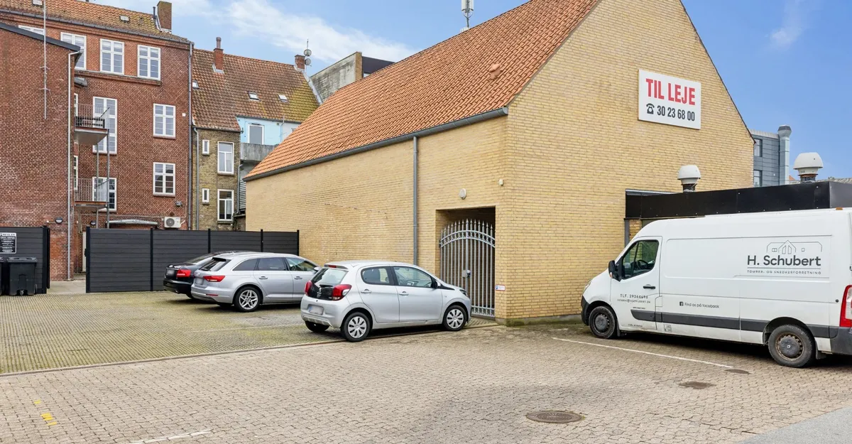 Parkerede biler og en hvid H. Schubert-lastbil i en forretningszone i Sønderborg