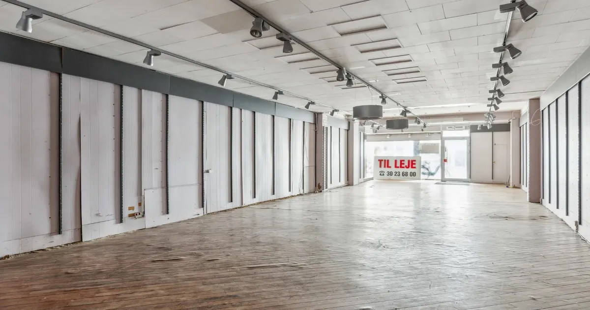 Kortere række af tomme butikker med hvide vægge og lyse lofter med sporlys og et skilt med teksten Til Leje.