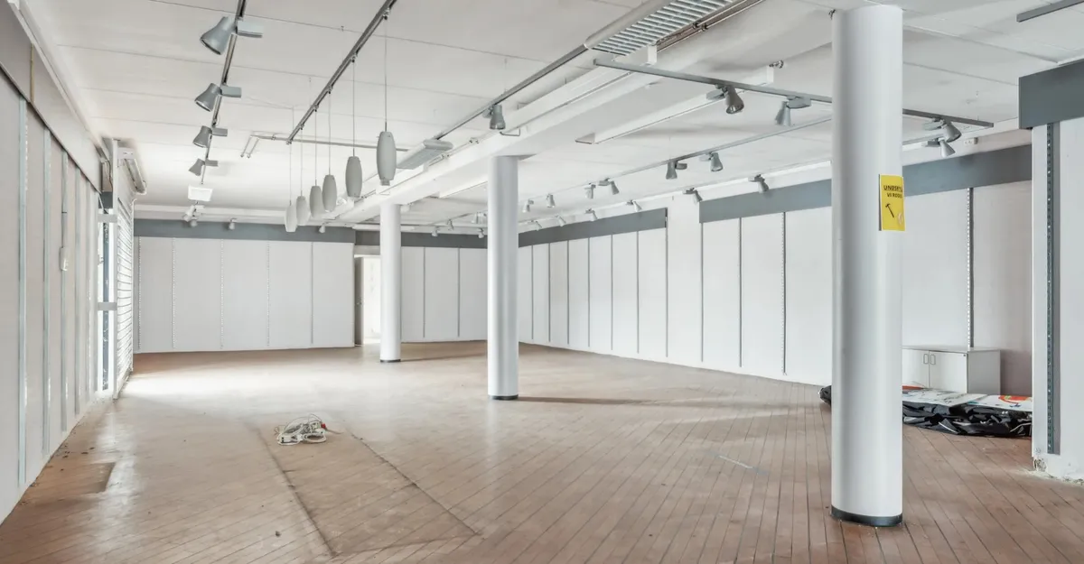 En stor og tom lejemål med hvide vægge, højt loft og moderne belysning. I gulvet er der en stor åbning og en