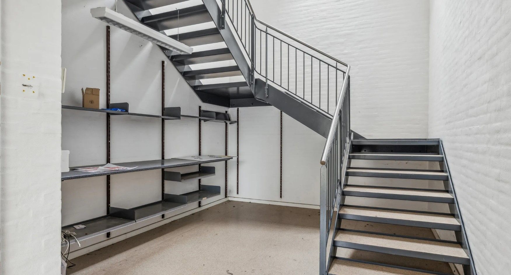 Moderne, minimalistisk lager med loftsrum, integreret trappe og lyse loftslamper, der skaber et rummeligt og velorganiseret
