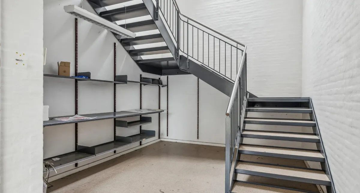Moderne, minimalistisk lager med loftsrum, integreret trappe og lyse loftslamper, der skaber et rummeligt og velorganiseret
