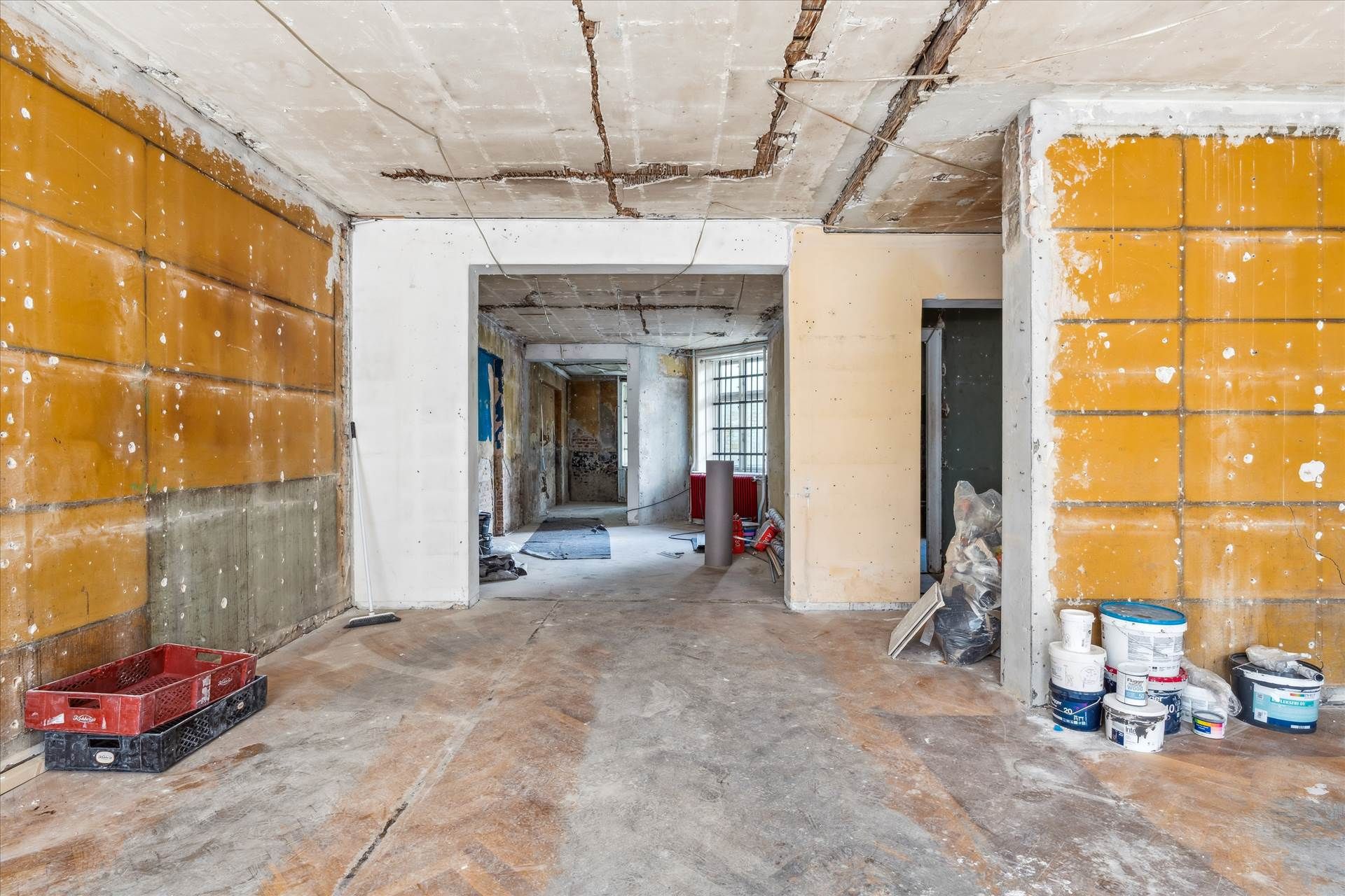 Rå værelse med gule vægge og mange skrald. Malermaterialer og krate på gulvet