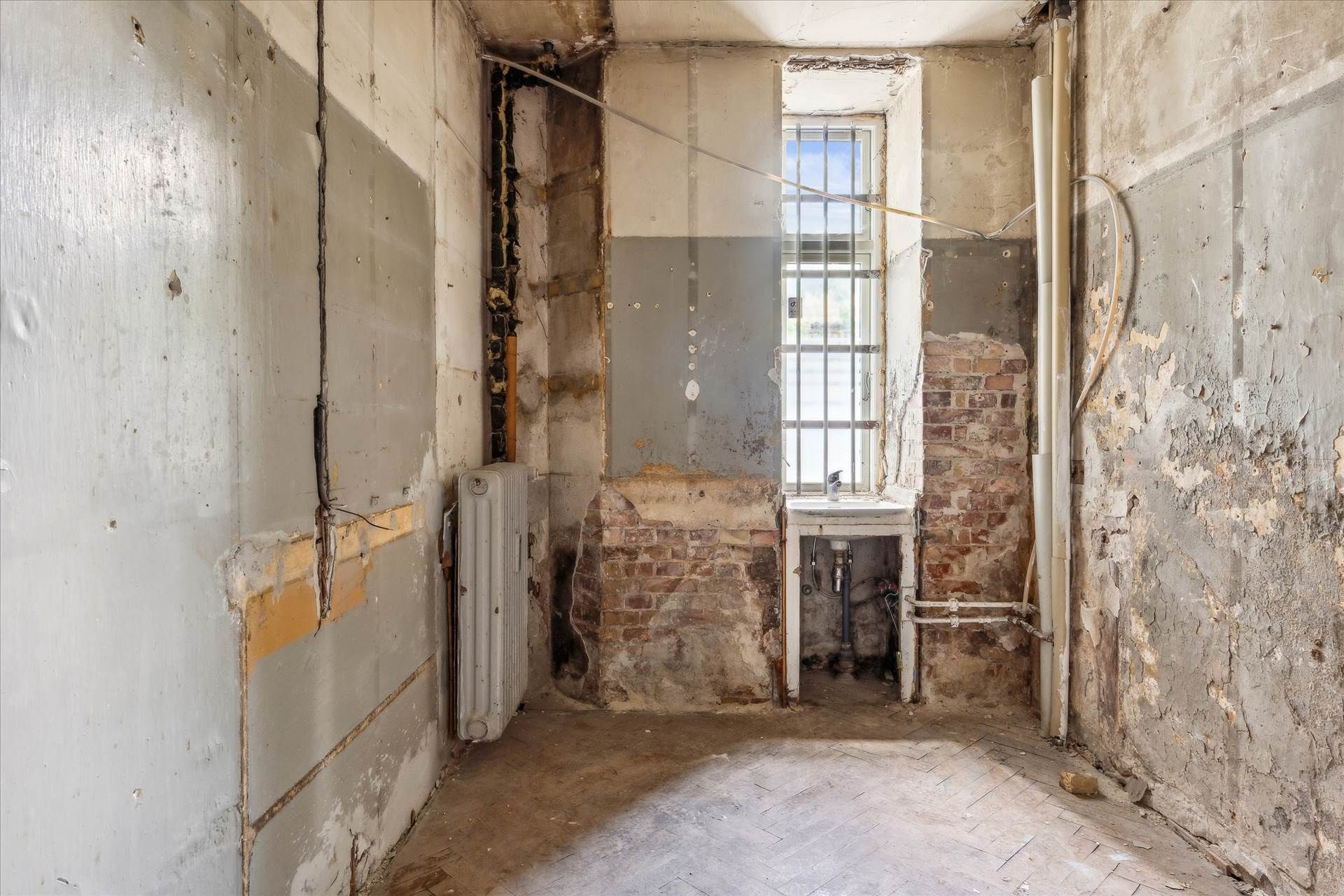 Et forladt og renoveringsbehovsfyldt rum med skrapelister og skadet gulv, hvor et sammenbrudt skur og røgskader er synlige.