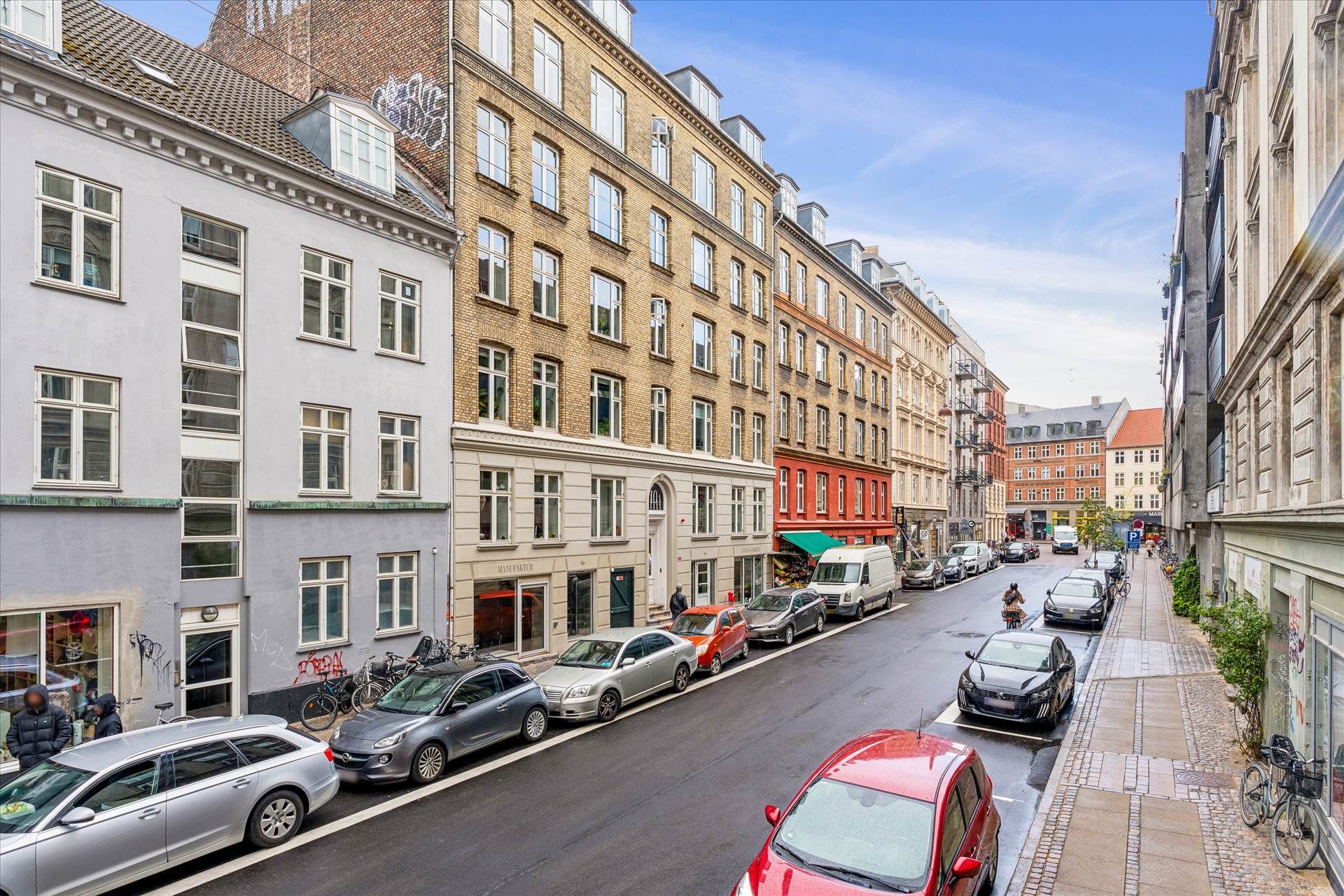 Flere biler parkeret på Griffenfeldsgade med fortov og cykler, mens en cyklist kører langs siden