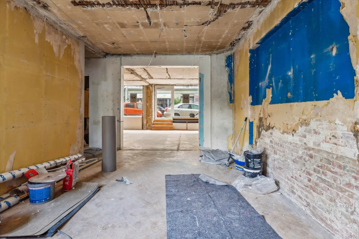 Rå værelse med skadet væg og loft, to bøtter og to ruller tapet, gulvrensende værktøj og støvsuger