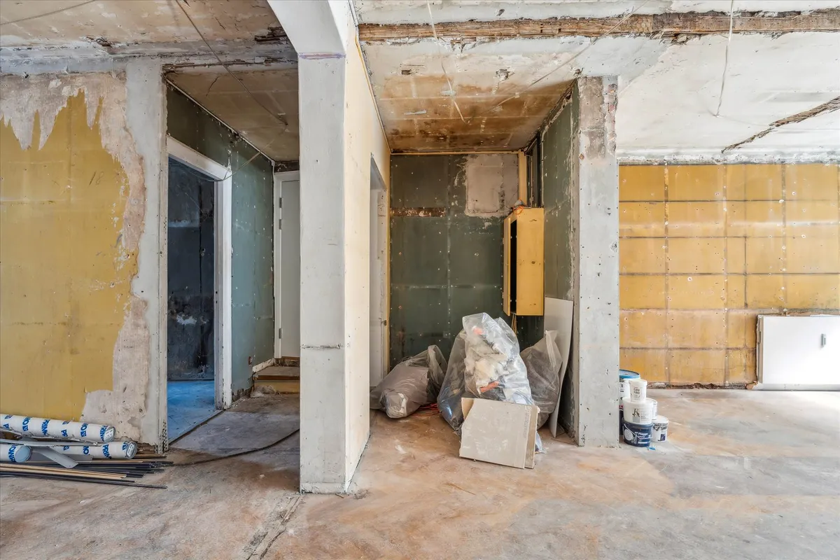 En renoveringszone med trægulve, søjler og skade på vægge og loft. Stykker og poser er samlet på gulvet.