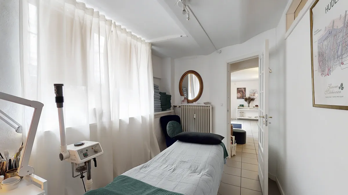 Et rum med et hvidt sengetøj, en komfortabel seng og et lille skrivebord med et hængende apparat