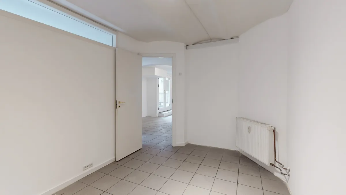 En tom og hvidmalet butikslokale med åben dør og tæt ved radiatoren og en indgangsdør med vinduesglas.