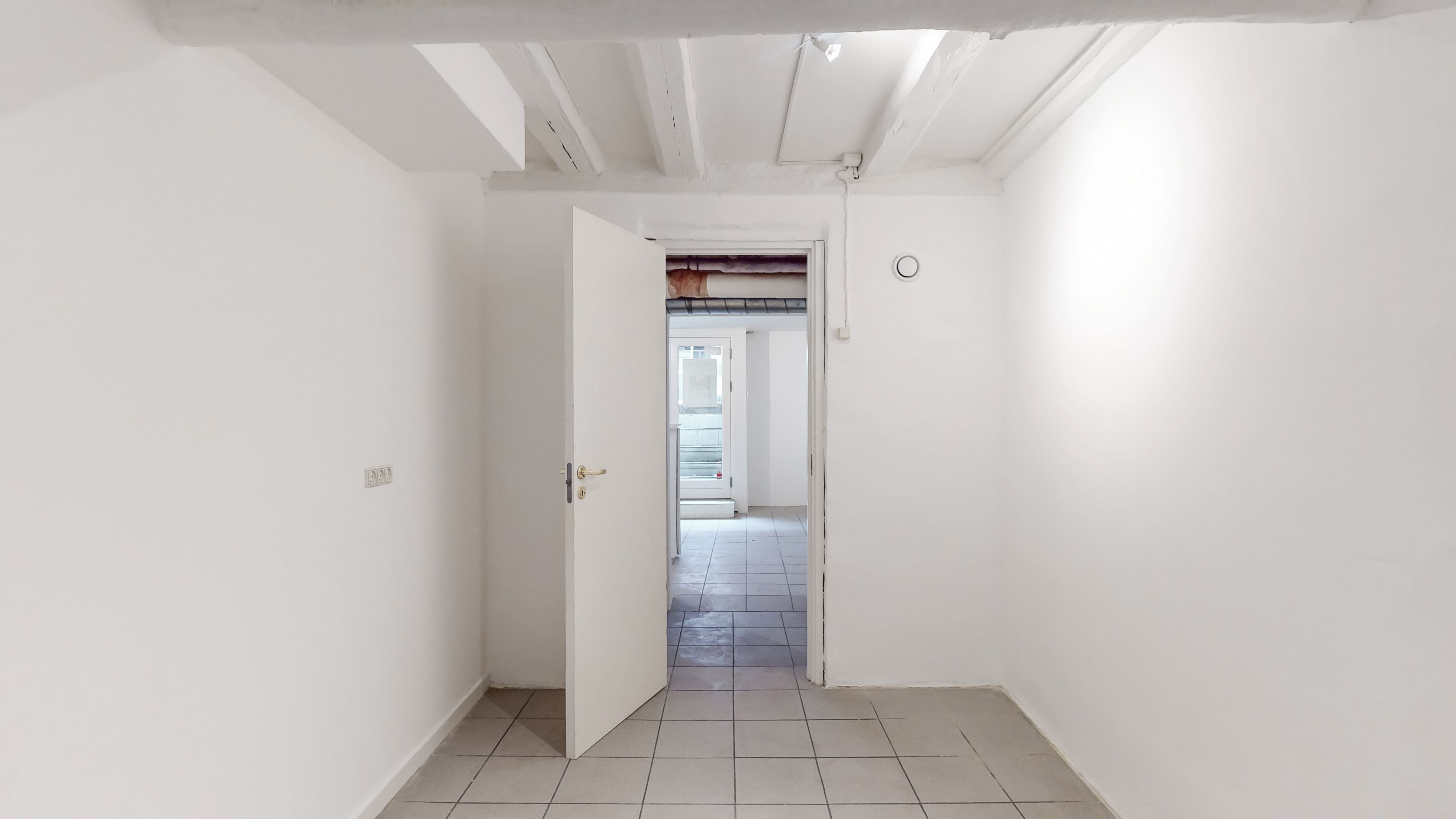 Moderne butikslokale med hvidt loft og gulv samt åben dør i København K. Lokalet er lyse og rent med gult lys fra loftet