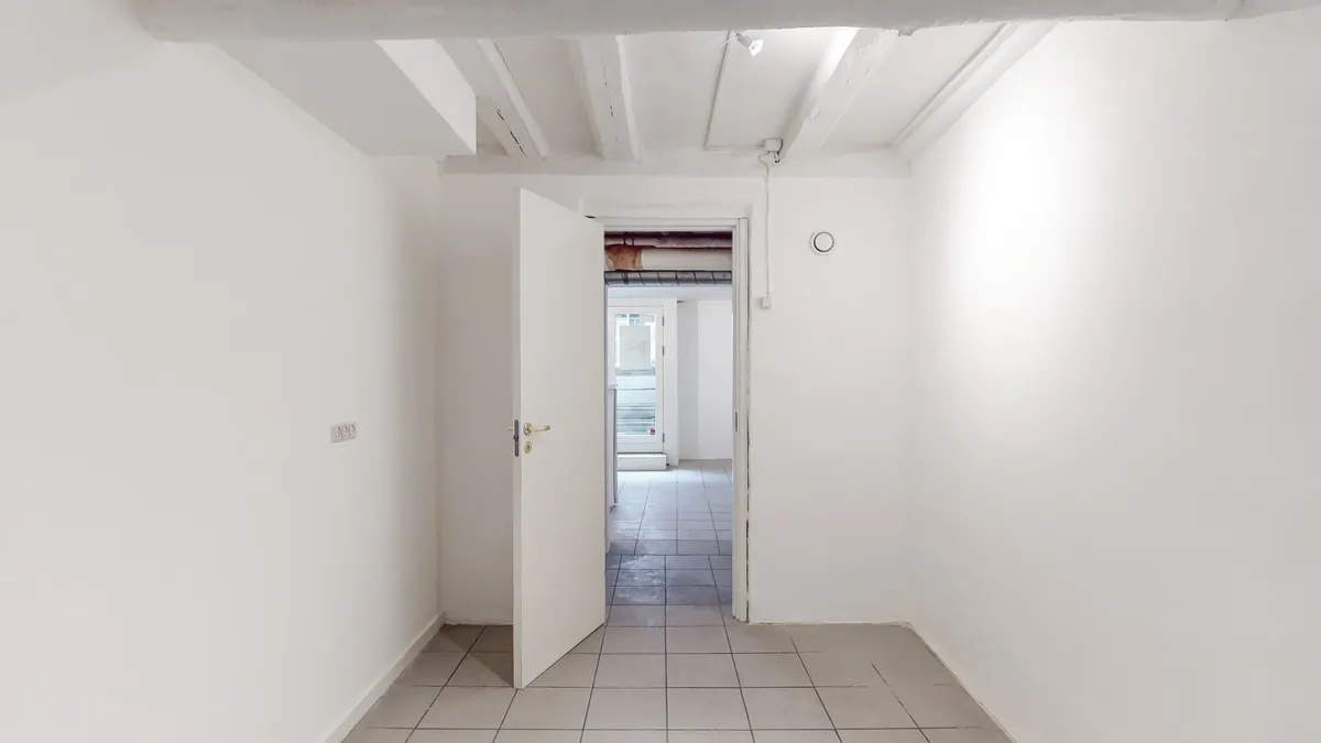 Moderne butikslokale med hvidt loft og gulv samt åben dør i København K. Lokalet er lyse og rent med gult lys fra loftet