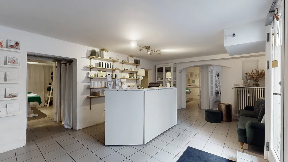 Hvidt, minimalistisk kontorlokal med stol, sofa, høj gulvbelægning og hylder med produkter.