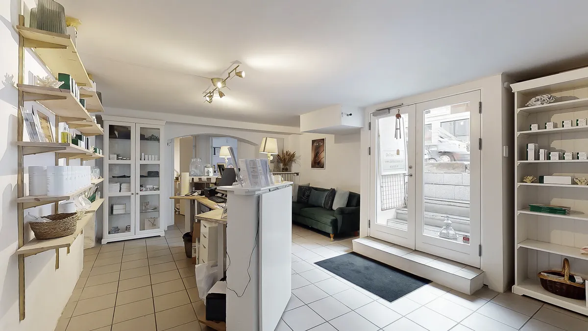 Nyd det hyggeligt indrettede forretningslokale med hvidt loft og gulv samt hyggelige møbler og lyse loftslampe. Stå ved