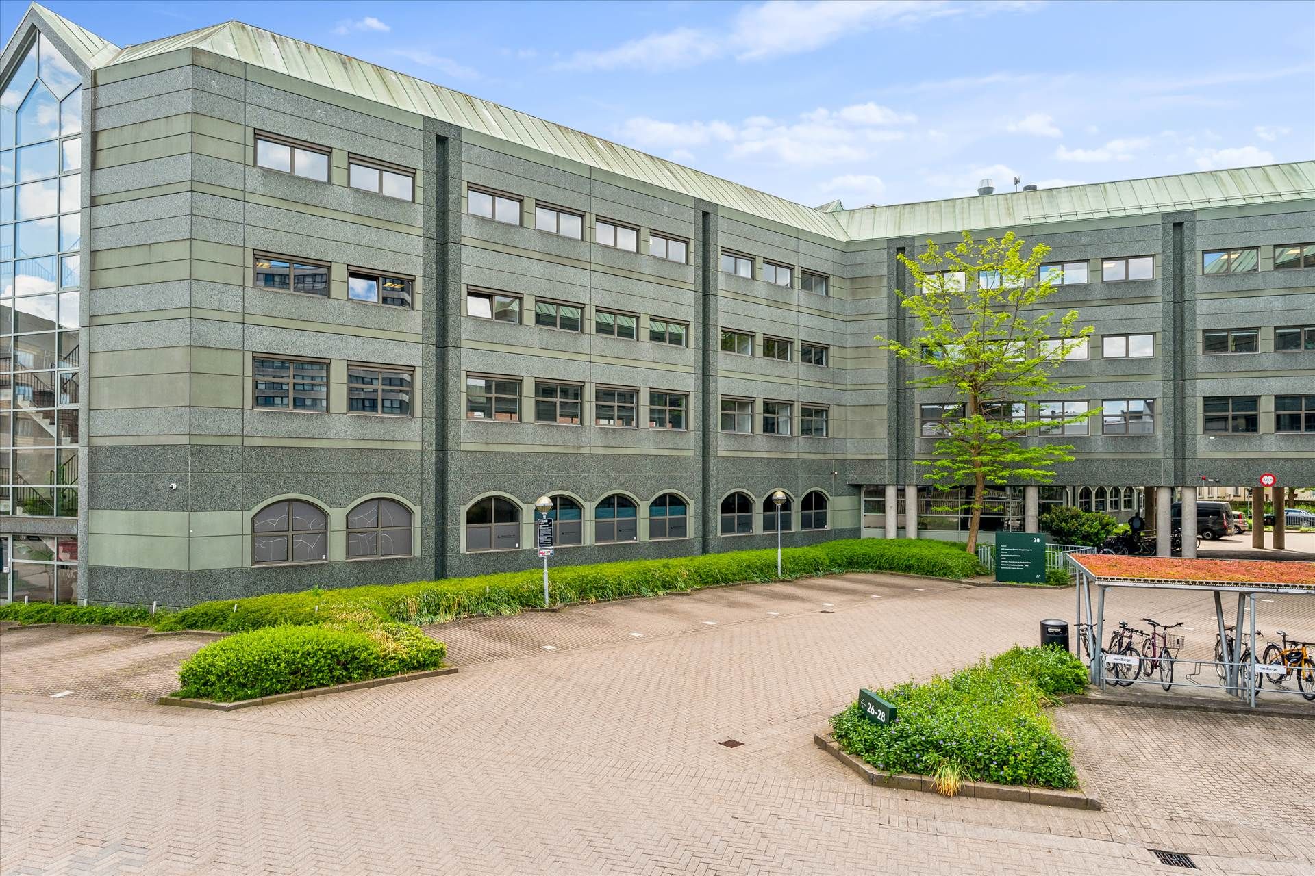 En moderne bygning med glasvinduer og grønne buske foran er et sundhedscenter i Bryggervangen