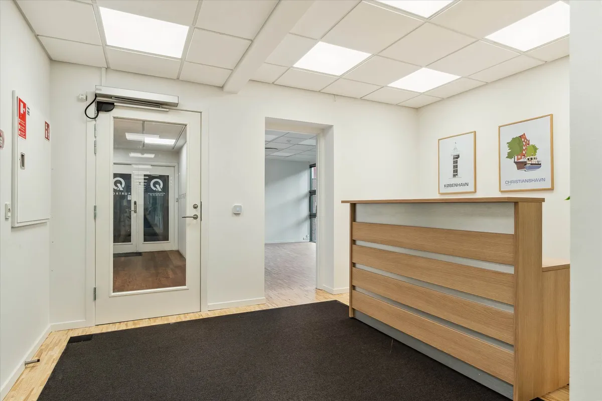 en moderne lobby med en hvid væg, et trægulv og en høj, lysegrå bordplade med to malerier bagved